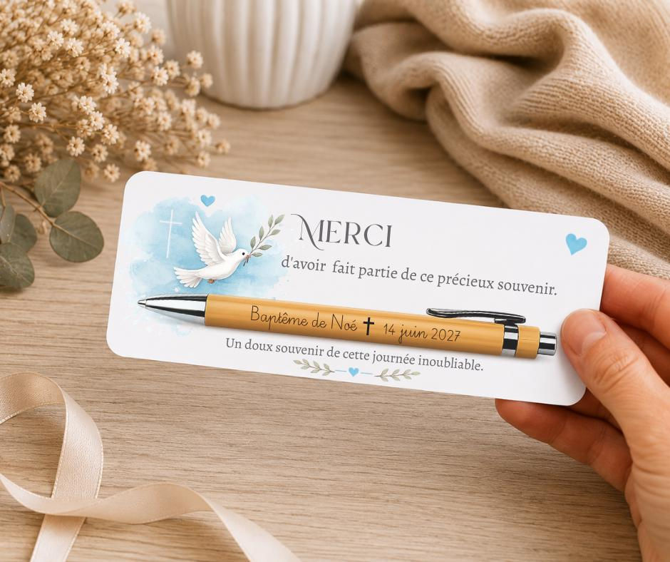Peut inclure: Un stylo à bille en bois brun clair avec un clip noir, fixé sur une carte rectangulaire blanche ornée d'une colombe à l'aquarelle bleue, d'une croix et du texte : MERCI d'avoir fait partie de ce précieux souvenir. Baptême de Noé 14 juin 2027.
