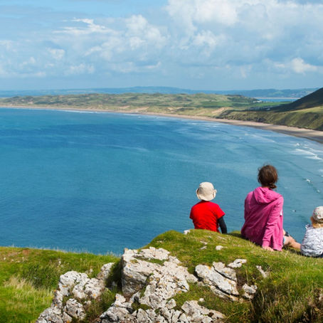 A family sitting on a clifftop overlooking a beach.  