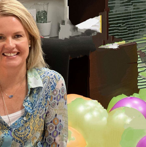 Danielle Legg, Smiling , in a colorful patterned shirt sits in an office chair. Background filled with colorful balloons and cluttered desk items.