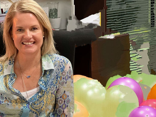 Danielle Legg, Smiling , in a colorful patterned shirt sits in an office chair. Background filled with colorful balloons and cluttered desk items.
