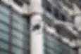 A drone flies near a modern building with grid-patterned glass windows and pipes. The scene is industrial with a focus on technology.