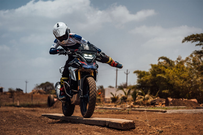 Motorcyclist on blue and black motorcycle navigating a wooden beam in sunny outdoor area