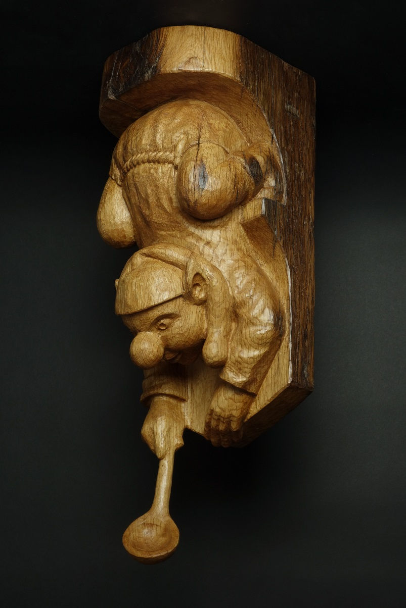 Lutin se penchant dans le vide pour attraper quelque chose avec sa cuillère. Sculpture en bois de Christian Delacoux.