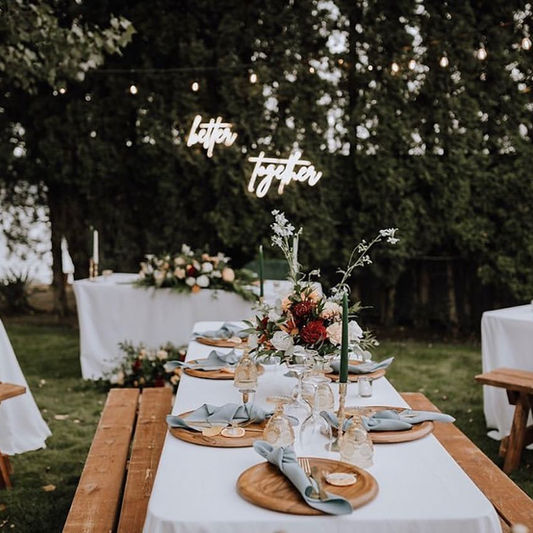 Outdoor table setup with “Better Together” neon sign and floral centerpieces
