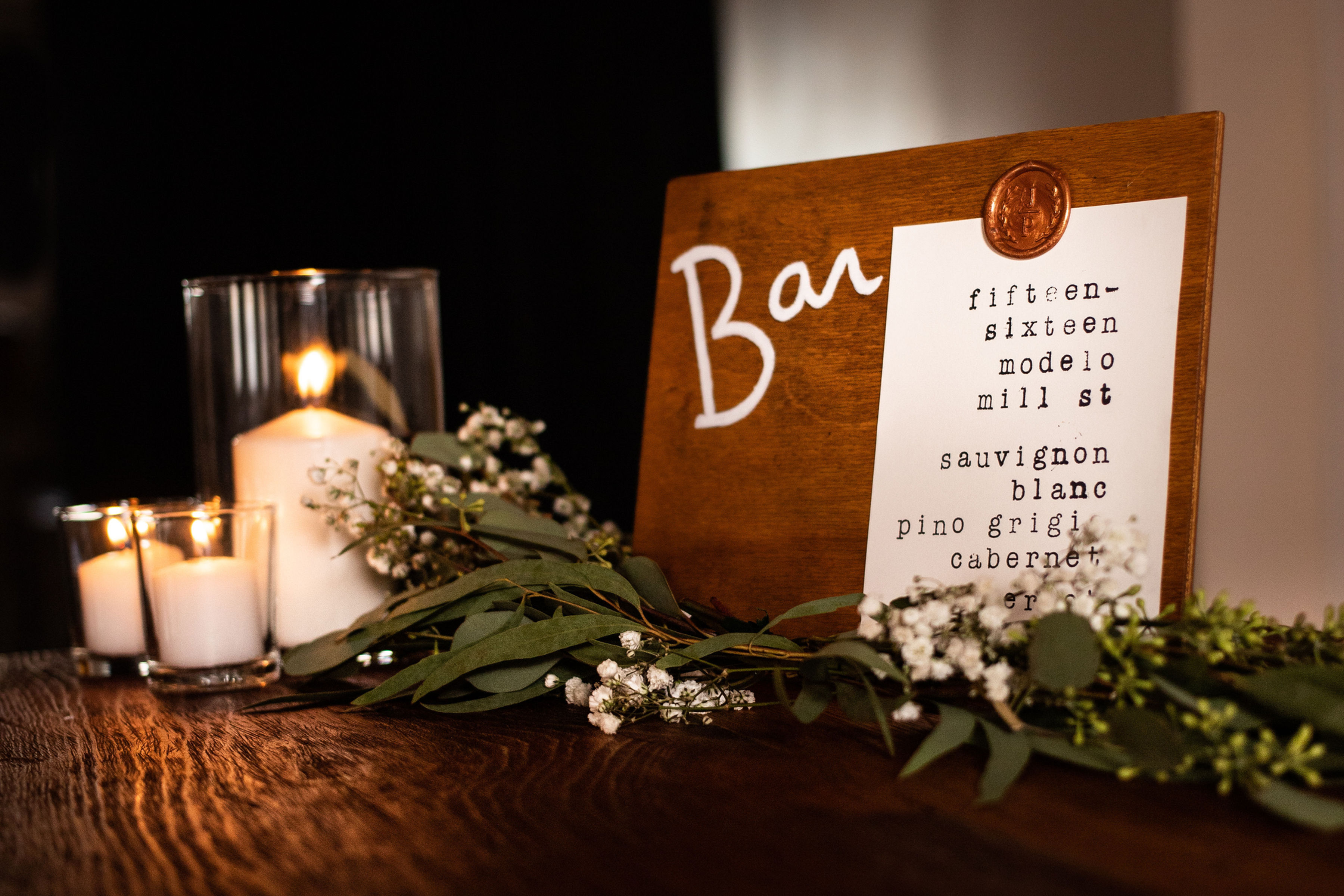 Small wooden sign that says bar with a paper waxed sealed to it, listing the bar menu