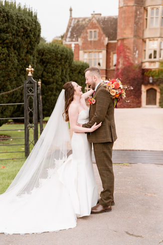 Bride and Groom standing together outside the grand entrance of St Audries Park, with veil flowing in the breeze