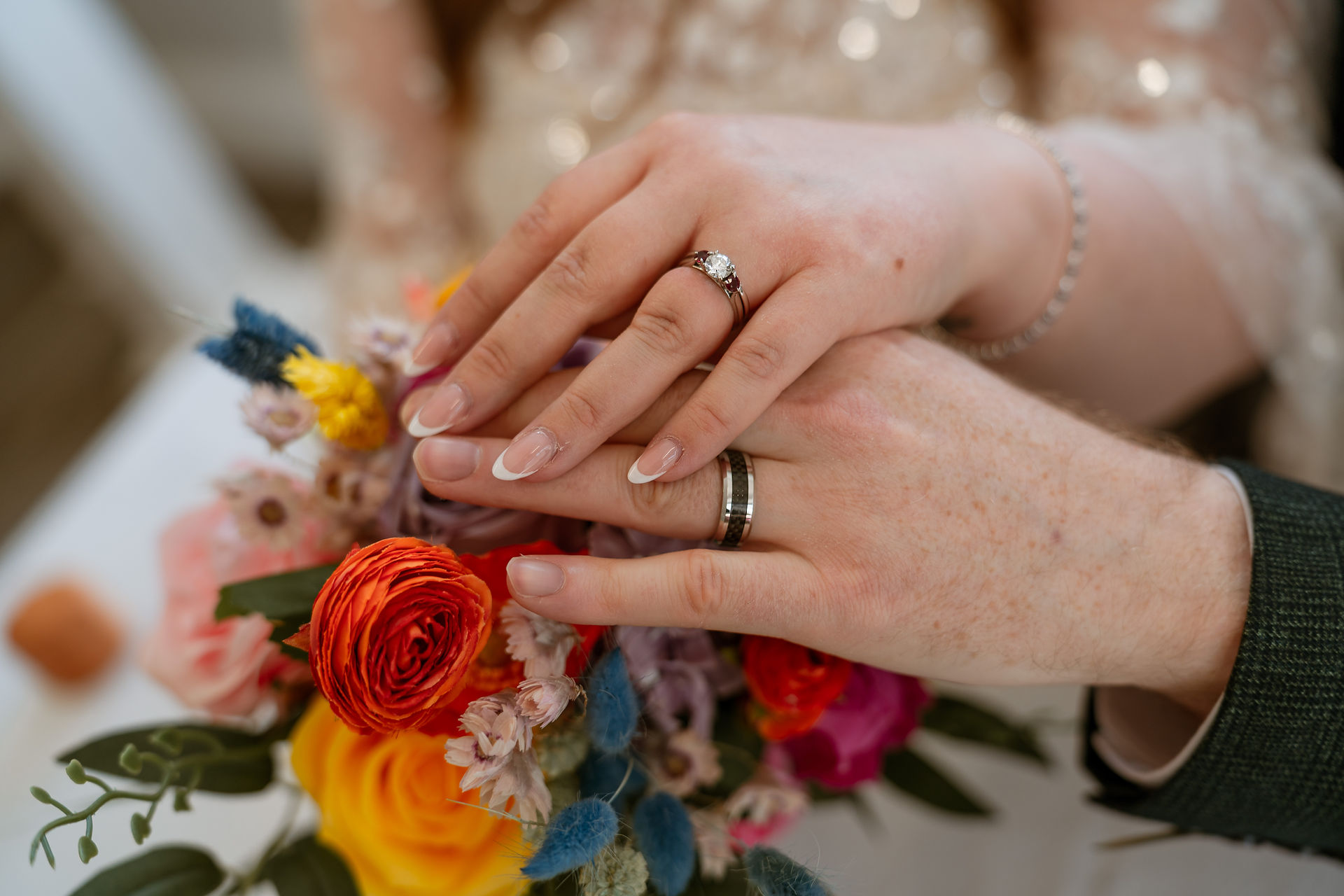 Colourful wedding bouquet with bright, seasonal flowers and the couple holding over their wedding rings
