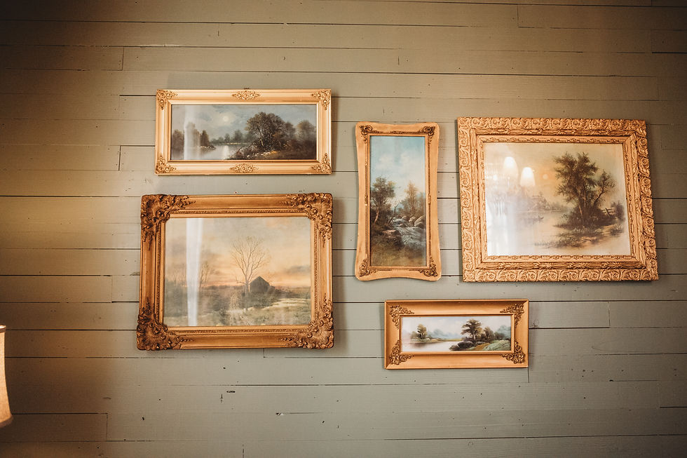 Antique landscape paintings in ornate gilded frames displayed on original green tongue-and-groove walls in the parlor of an 1898 Victorian farmhouse.