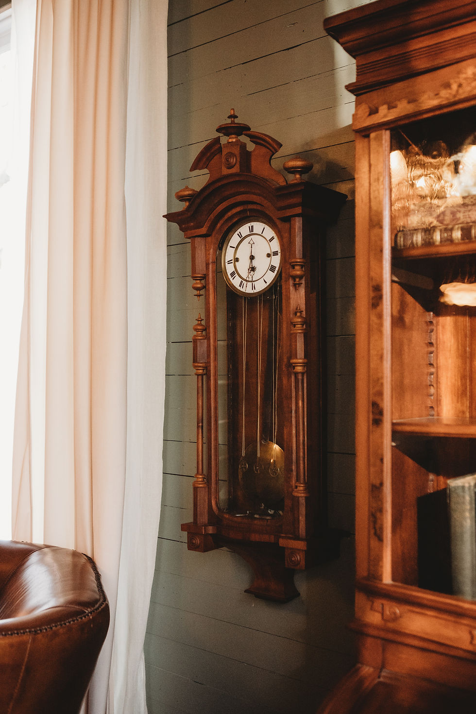 Antique wall clock mounted on original green tongue-and-groove walls beside an Eastlake secretary desk in the parlor of an 1898 Victorian farmhouse.