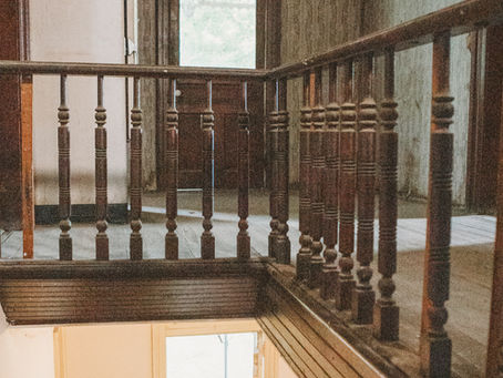 Second-story hallway railing in 1898 Victorian famhouse showing original wood spindles and transition from painted to exposed wood