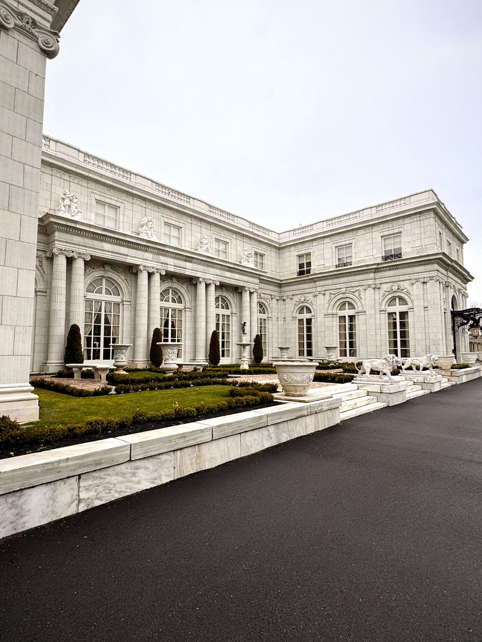 Exterior of Rosecliff Mansion in Newport, Rhode Island, featuring white stone architecture, columns, arched windows, and formal gardens on an overcast day.