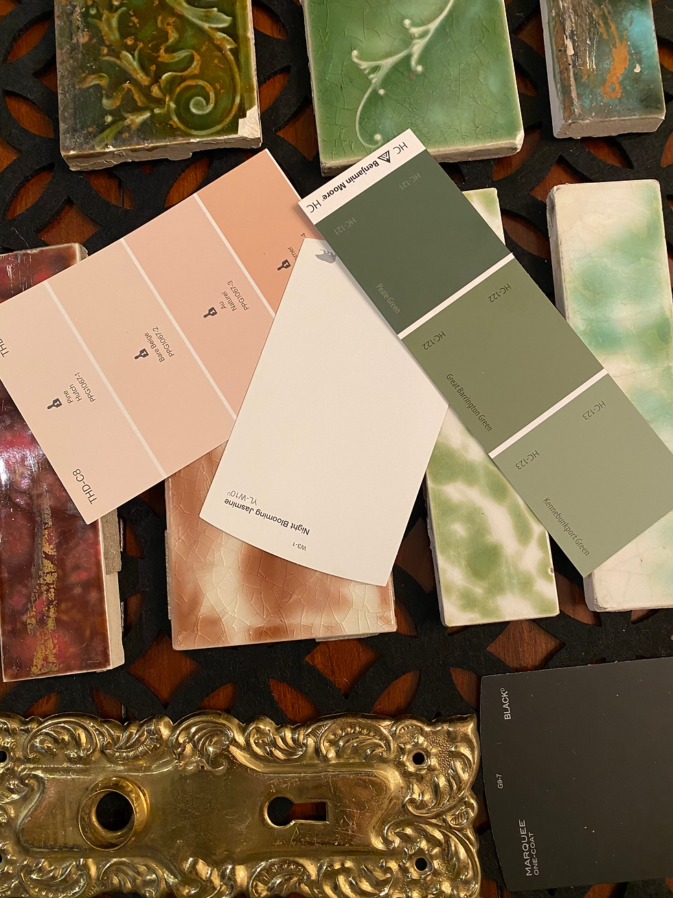 Paint swatches and glazed tile samples in greens, peach, and black, with a gold ornate plate and labels scattered on a table.