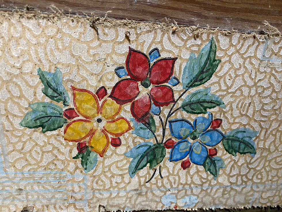 Close-up photograph of a vintage floral wallpaper fragment discovered during the restoration of an 1898 Victorian farmhouse. The wallpaper features hand-painted style red, yellow, and blue flowers with green leaves on a textured cream background.