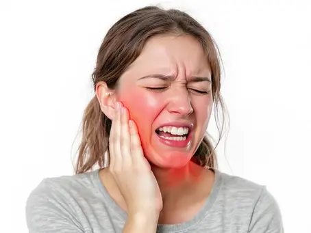 Woman in pain, clutching her cheek with a red, inflamed area. She's wearing a gray shirt against a white background, eyes closed.