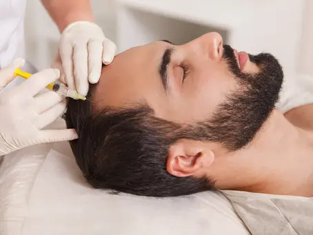 Person receiving scalp injection from gloved professional. Lying on white sheet, eyes closed. Calm setting, close-up view.