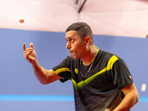 Coach Shahin Akhlaghpasand intensely focused while hitting a forehand shot during a table tennis match.