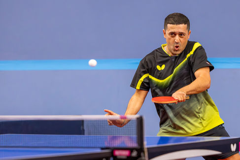 Coach Shahin Akhlaghpasand intensely focused while hitting a forehand shot during a table tennis match.