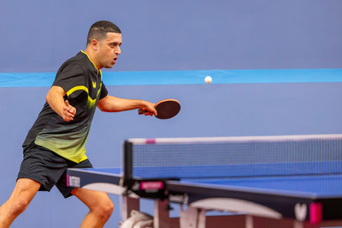 Coach Shahin playing table tennis at the ATTC Mega Money Open, intensely focused on the ball mid-flight