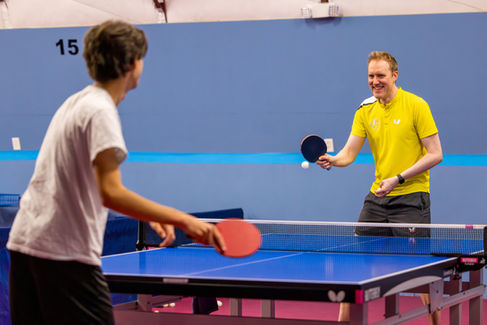 Coach Clayton Pavlicek smiles enthusiastically while playing table tennis with a student at the Austin Table Tennis Club.