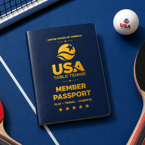 A dark blue USA Table Tennis Member Passport with gold text and logos, resting on a blue table tennis table. The passport reads "Member Passport: Play, Travel, Compete" above five gold stars. A table tennis net, the edges of two paddles, and a white ping-pong ball featuring the USA Table Tennis logo surround the passport.