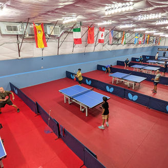Interior view of Austin Table Tennis Club showing active table tennis courts and international flags.