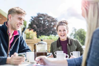 • Lifestyle brand photography showing a man and woman smiling over morning coffee and tea during an outdoor breakfast meeting.