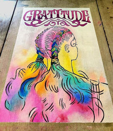 Chalk art of the back of a female head with rainbow colored hair in braids and purple word Gratitude in ornate lettering in Wheat Ridge Colorado.