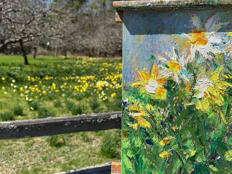 Painting of yellow flowers on an easel against the backdrop of a meadow with trees and yellow flowers. 