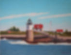 Lighthouse on rocky shore with red-roofed houses in the background, a flagpole, blue sky, and ocean waves. Peaceful coastal scene.
