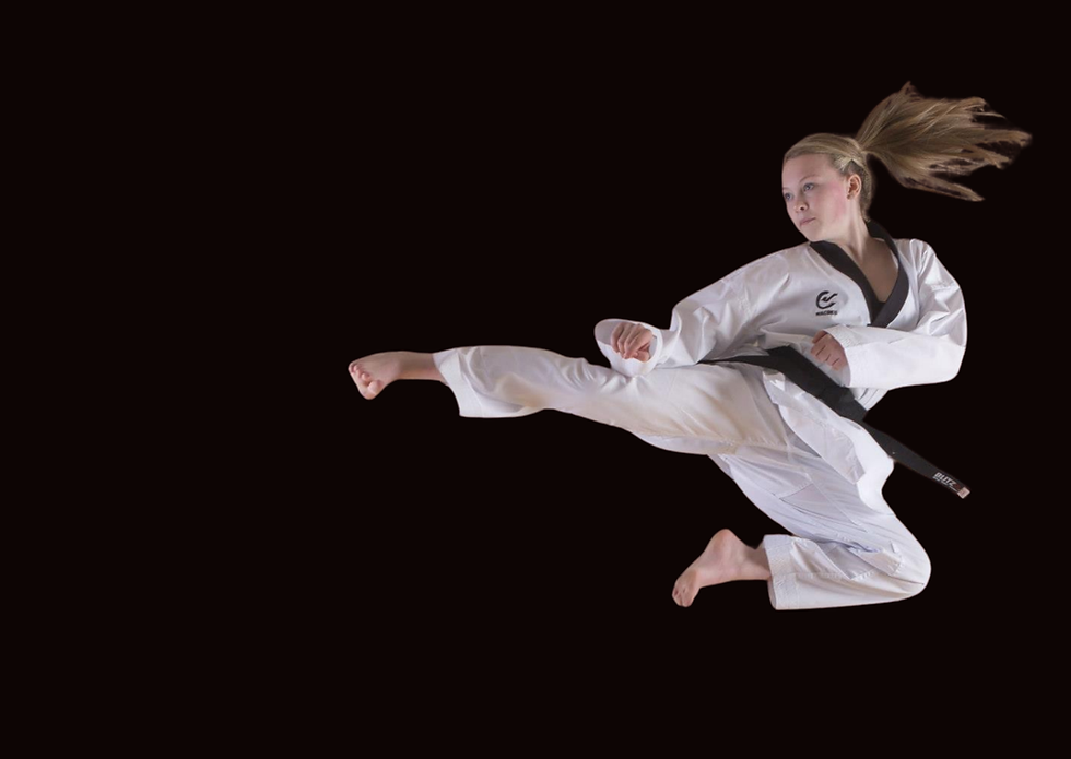 Young female student of Tan'Gun Martial Arts Academy in white taekwondo uniform performing a flying side kick.