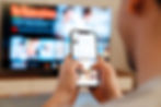 Adult male looking at smartphone with TV on in the background