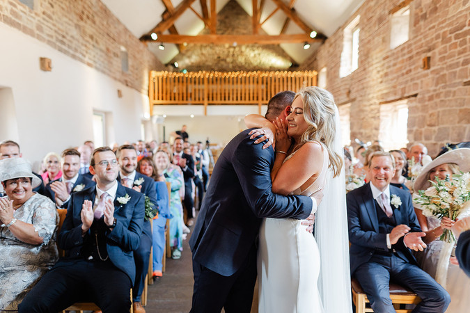 Photo of bride and groom hugging during their ceremony after their first kiss at The Ashes Barns wedding venue Stoke-on-Trentceremony at The Ashes Barns Wedding Photography