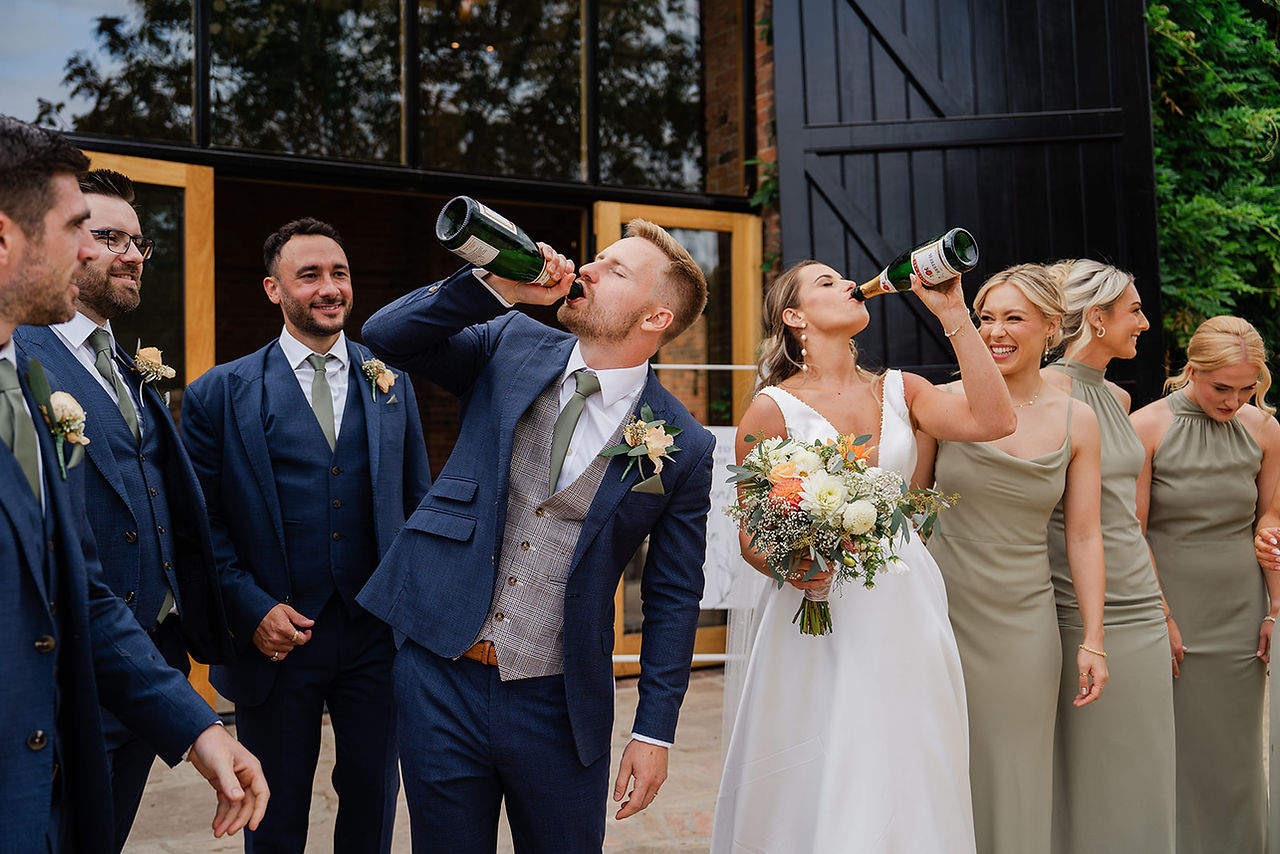 Bridal party and groomsmen celebrating with champagne outside The Mill Hoveringham. Fun and candid wedding photography.