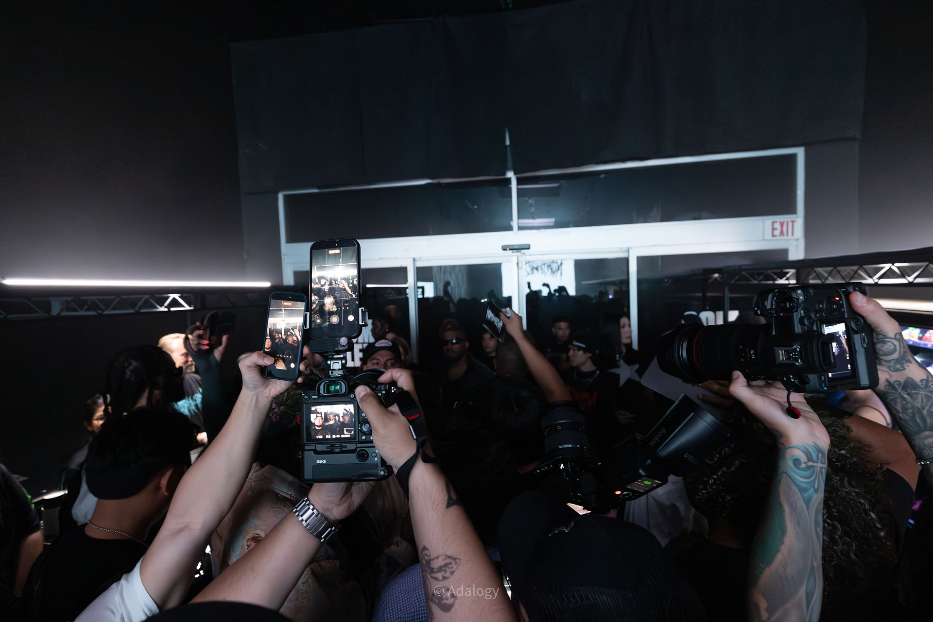A group gathers together to take pictures of artist Kanye the crowd is seen around him in a darker room while cameras are photographing all of them