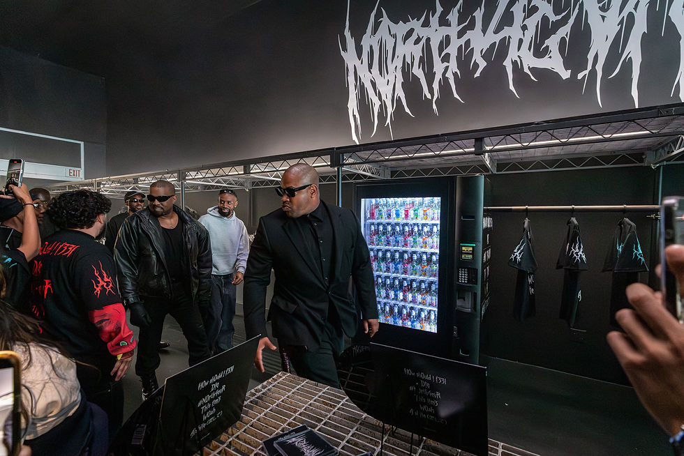 Artist Kanye west is arriving wearing a black leather jacket in front of him is a bodyguard wearing all black looking at the crowd 