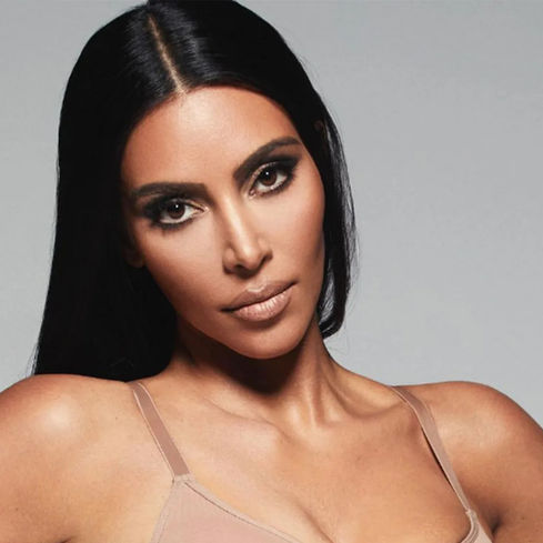 Kim Kardashian posing in nude Skims shapewear against a plain gray background.