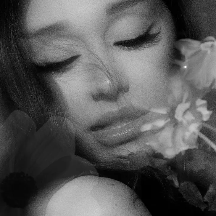Black-and-white close-up portrait of a woman, Ariana Grande, with closed eyes resting among flowers, used for the album’s pre-release song “Hate That I Made You Love Me.”