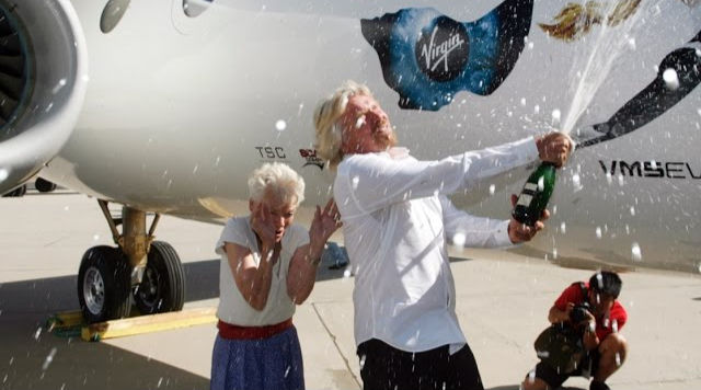 Richard Branson celebrating with champagne in front of a Virgin Galactic spacecraft, symbolizing the billionaire space race and private space travel.