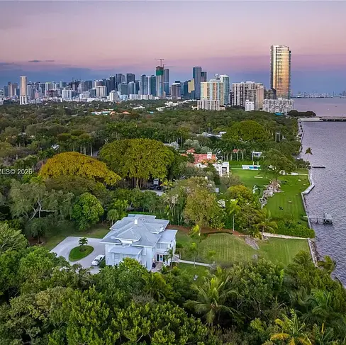 Elegant waterfront home at 3149 Brickell Ave Miami featuring private dock, expansive greenery, and panoramic Biscayne Bay views under blue sky.