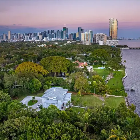Elegant waterfront home at 3149 Brickell Ave Miami featuring private dock, expansive greenery, and panoramic Biscayne Bay views under blue sky.