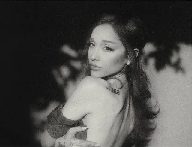 Black-and-white promotional image of Ariana Grande looking over her shoulder with soft lighting and a blurred background.