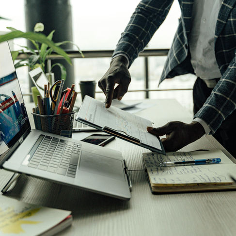 Two professionals in a modern office discuss a document with charts, surrounded by laptops, notes, and colorful pens — the universal signs of a “we’re totally crushing it” meeting.