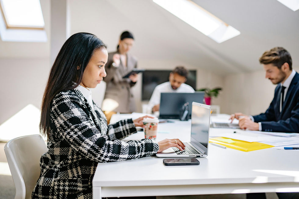 Professional team working together in a modern office space, with individuals using laptops and reviewing documents around a table.
