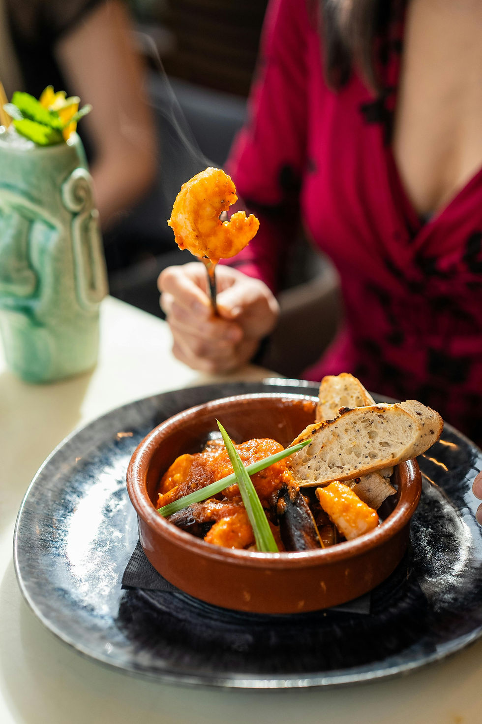 A person holding a steaming cooked shrimp over a bowl of shrimp stew with bread, highlighting the importance of checking shrimp sources amid the Walmart radiation recall.