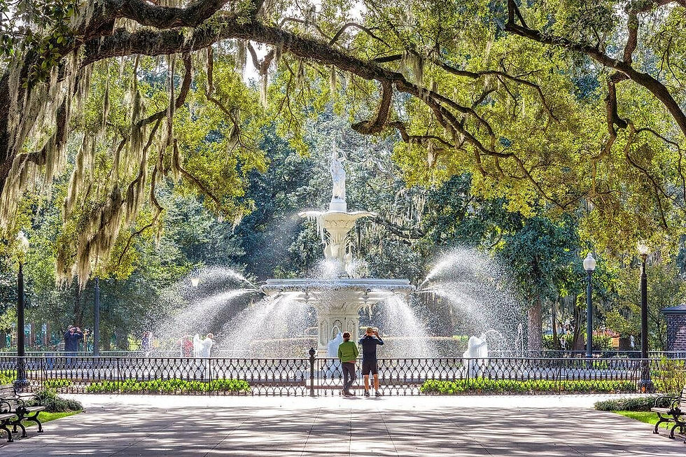 Forsyth Park Fountain in Savannah, Georgia, spraying water beneath sprawling live oak branches draped with Spanish moss as visitors stand near the railing.
