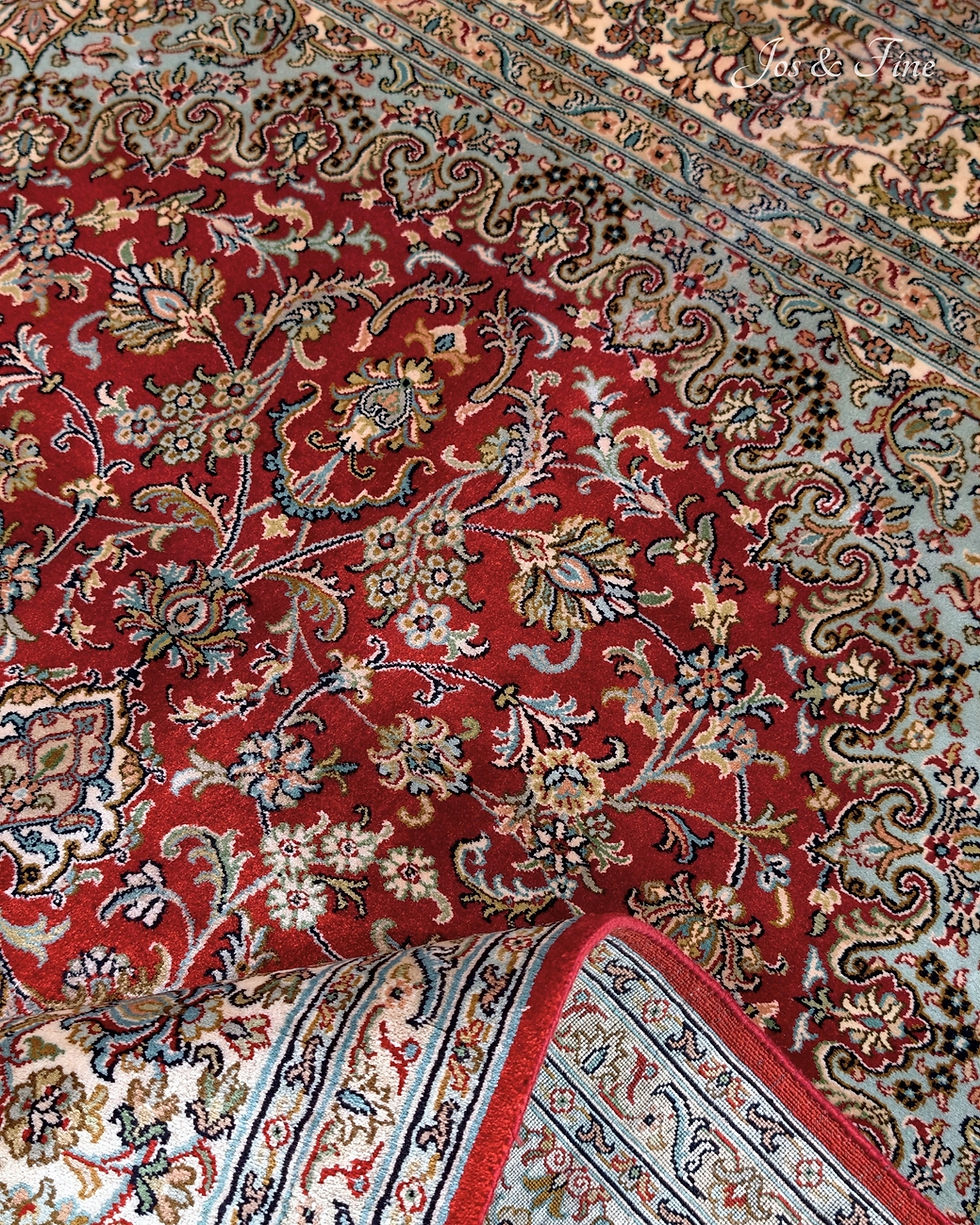 Thumbnail: Close-up of the detailed traditional crimson field arabesque pattern on a Kashmiri silk rug, with the back folded over.