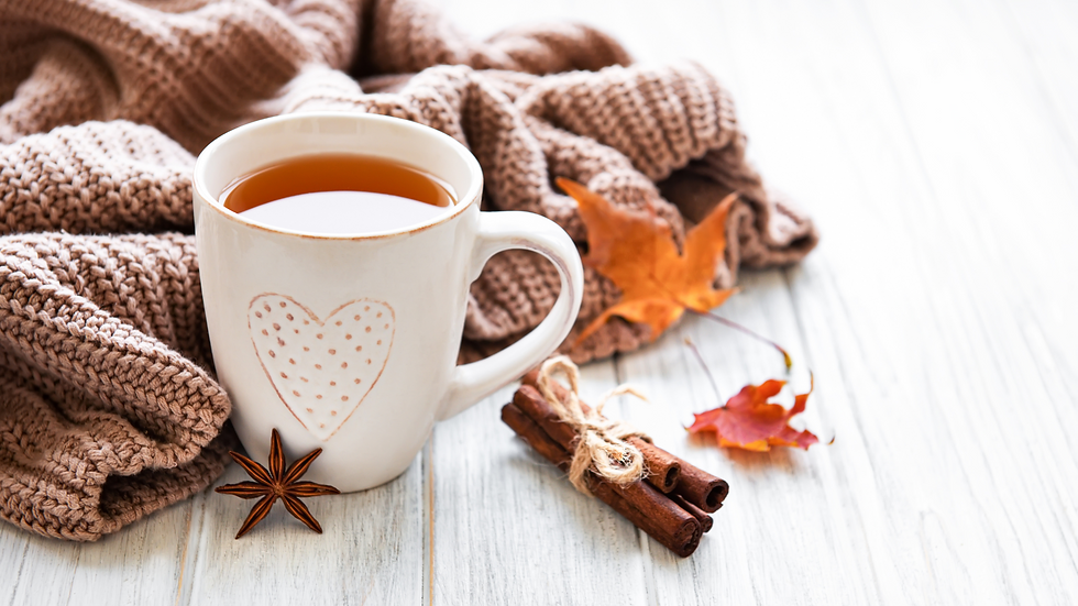 Cozy scene: white mug with heart, filled with tea; cinnamon sticks, star anise, and autumn leaves on a knit blanket and wood surface.