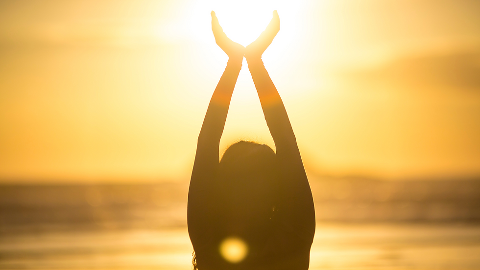 Silhouette of a person with arms raised against a glowing yellow sunset over the ocean, evoking a serene and peaceful mood.