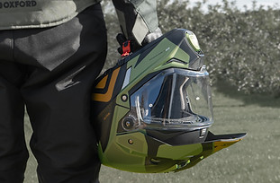 Product photography lifestyle image of a rider holding their helmet by the straps beside their leg.