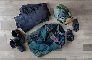 Product photography lifestyle flat lay of helmet, jacket, gloves, boots and trousers organised on a hardwood floor.